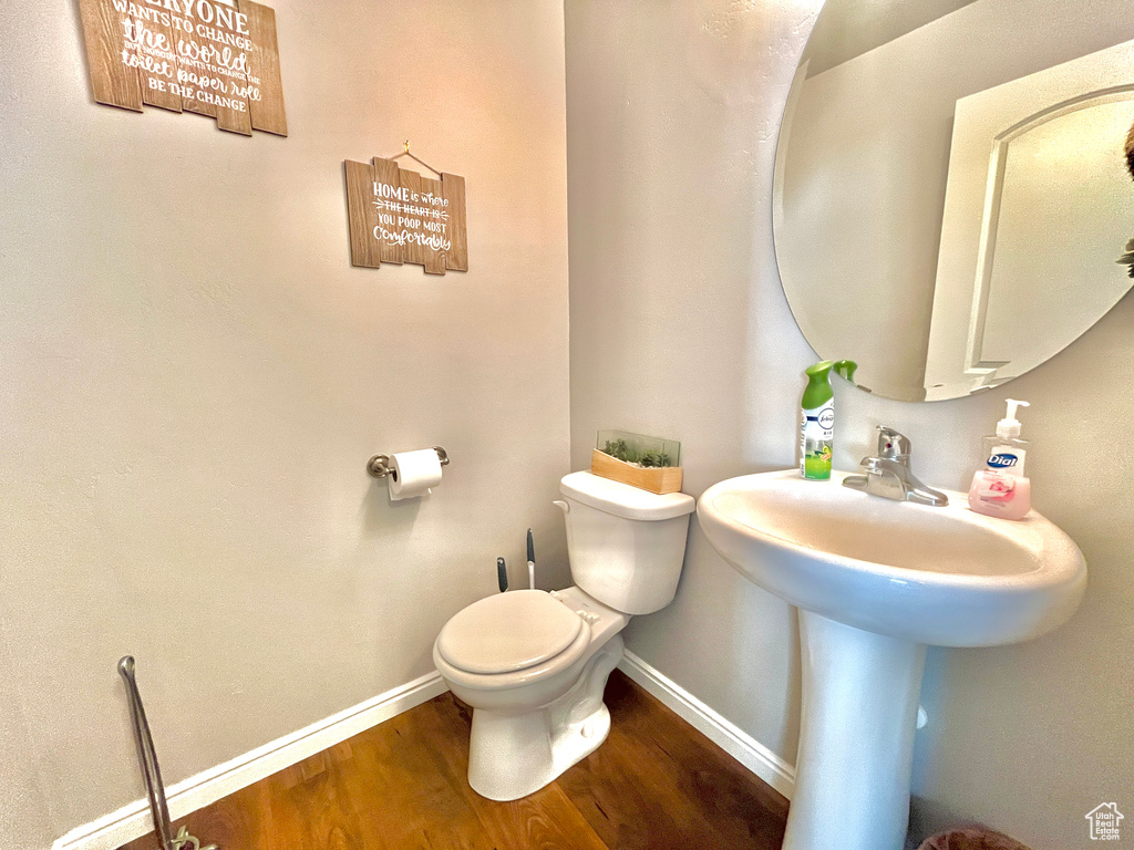 Half bath featuring wood finished floors, toilet, and baseboards
