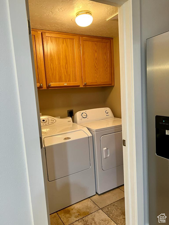 Laundry area with separate washer and dryer, cabinet space, and a textured ceiling