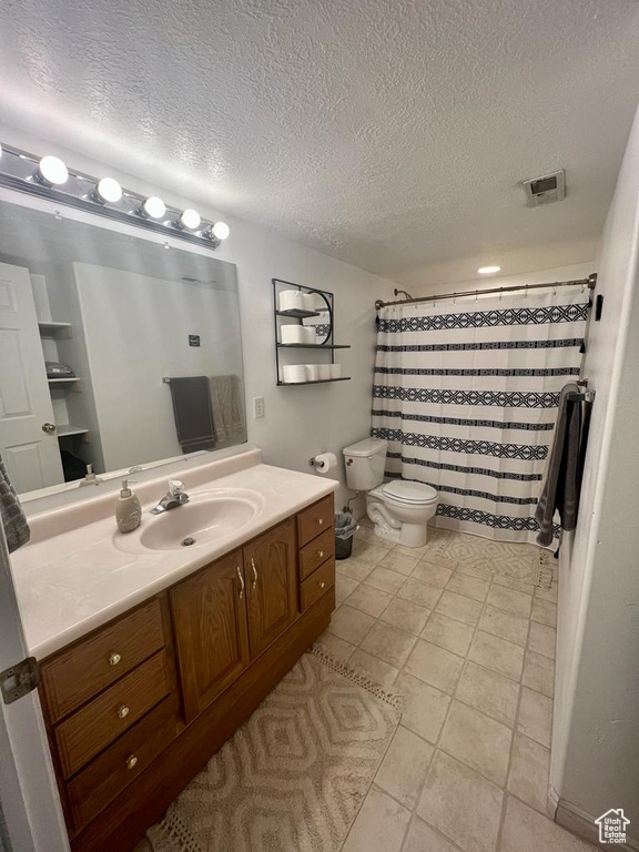 Full bath with a textured ceiling, vanity, toilet, tile patterned floors, and a shower with shower curtain