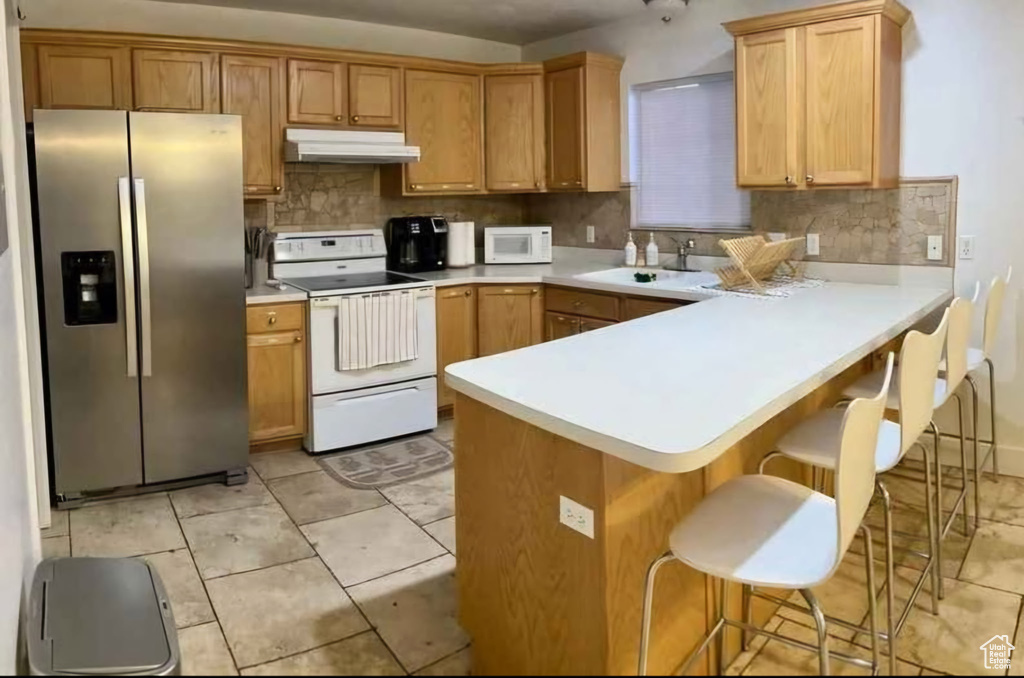 Kitchen with white appliances, under cabinet range hood, a peninsula, and light countertops