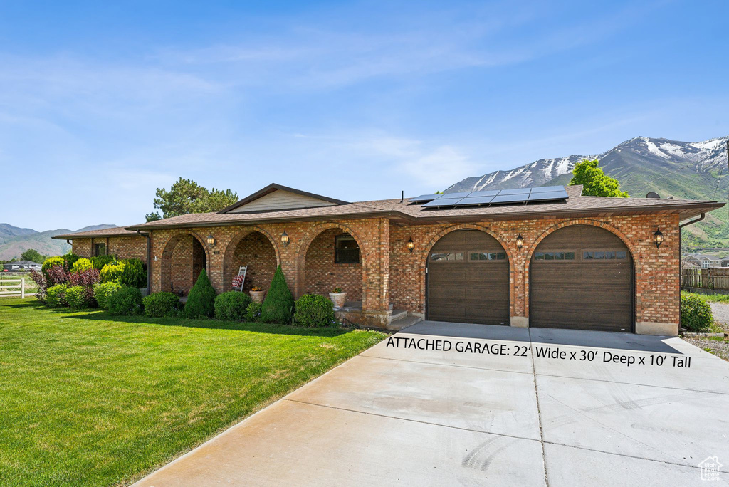 View of front of property featuring a mountain view, concrete driveway, an attached garage, a front lawn, and roof mounted solar panels