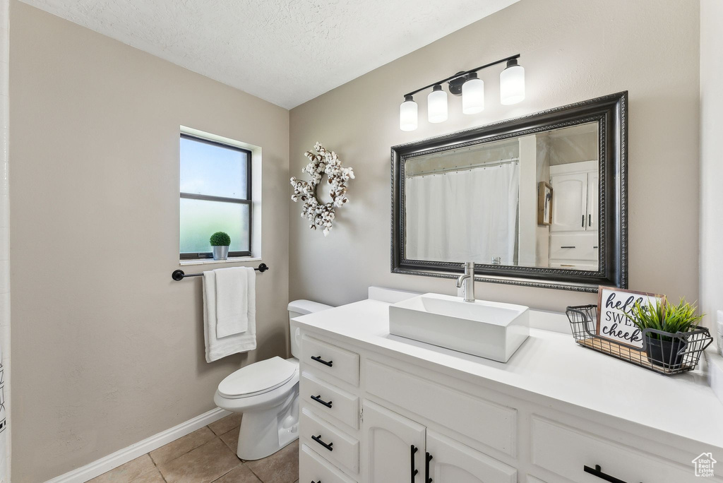 Full bathroom with toilet, a textured ceiling, tile patterned floors, baseboards, and vanity