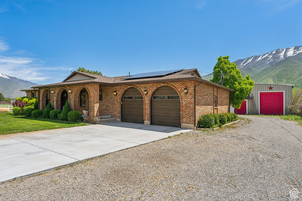 Ranch-style house with driveway, a mountain view, an attached garage, brick siding, and solar panels