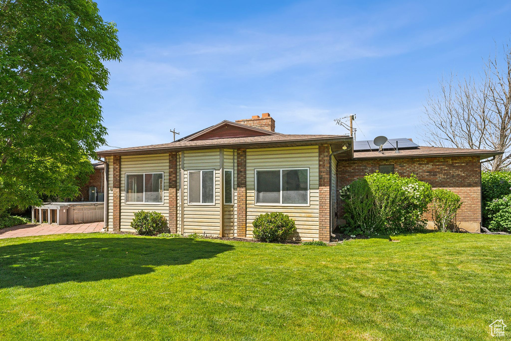 View of front of home featuring a chimney, brick siding, a front lawn, and roof mounted solar panels