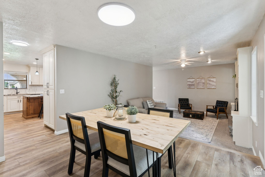 Dining space with a textured ceiling, light wood-type flooring, a ceiling fan, and baseboards