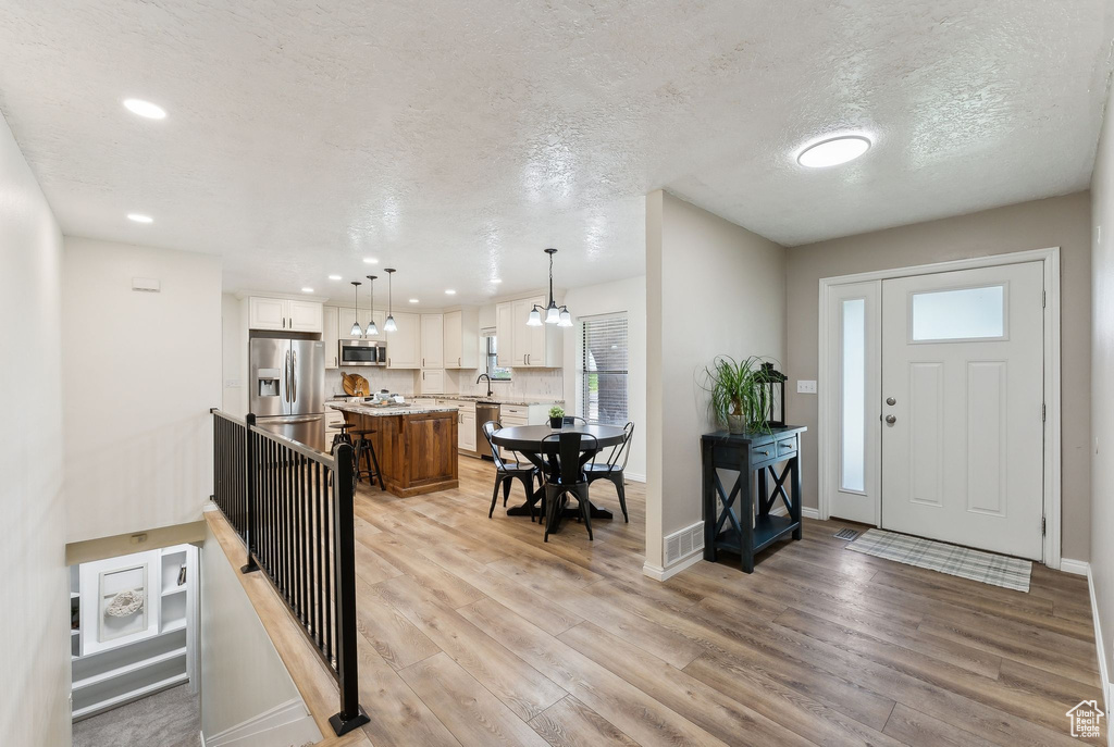 Foyer entrance with light wood-style flooring, baseboards, recessed lighting, and a textured ceiling