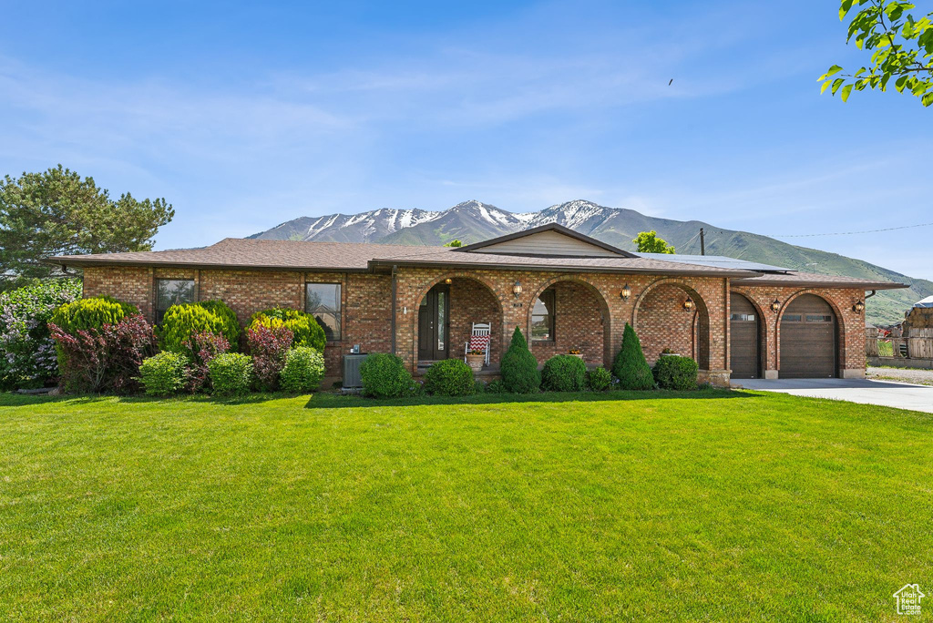 View of front of house featuring a mountain view, a front lawn, an attached garage, concrete driveway, and brick siding
