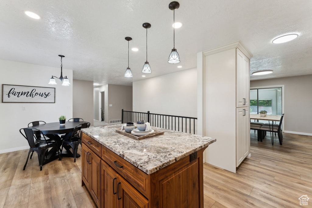 Kitchen featuring brown cabinets, light wood-style flooring, pendant lighting, a kitchen island, and recessed lighting