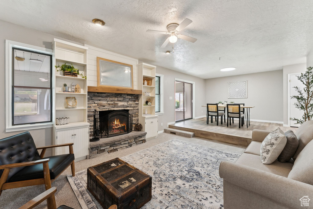 Living area featuring ceiling fan, a fireplace, a textured ceiling, baseboards, and light carpet