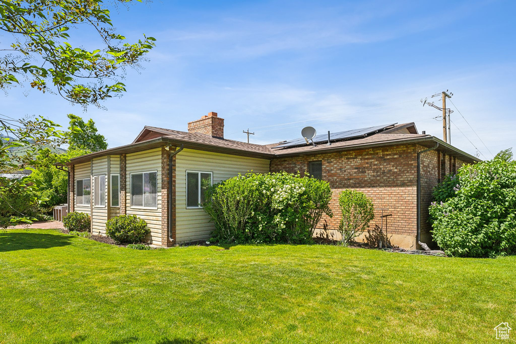 View of side of home featuring a chimney, a yard, roof mounted solar panels, and brick siding