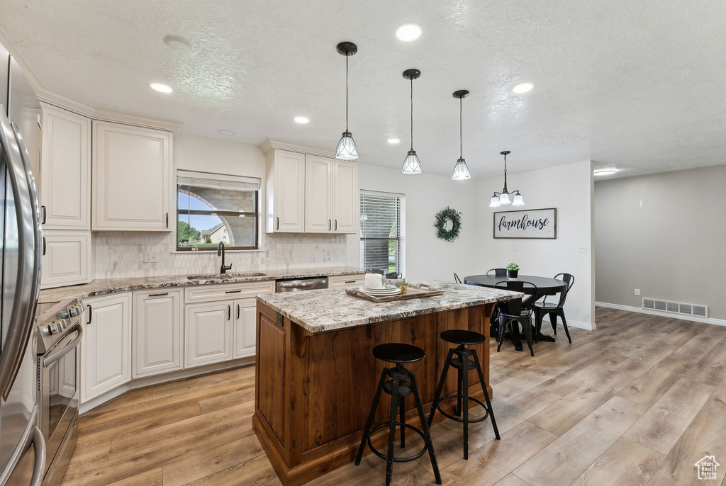 Kitchen with a sink, stainless steel appliances, decorative backsplash, a kitchen island, and light stone counters