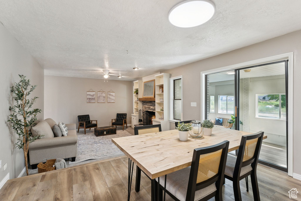 Dining room featuring a fireplace, ceiling fan, light wood-type flooring, a textured ceiling, and baseboards
