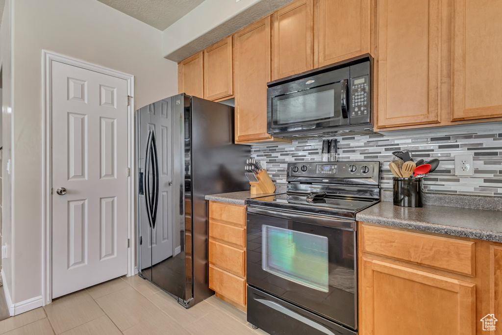 Kitchen featuring black appliances, backsplash, light tile patterned floors, and dark countertops