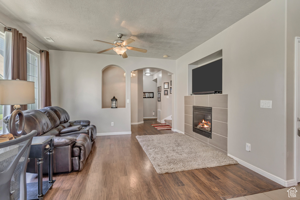 Living room featuring ceiling fan, arched walkways, baseboards, a textured ceiling, and wood finished floors