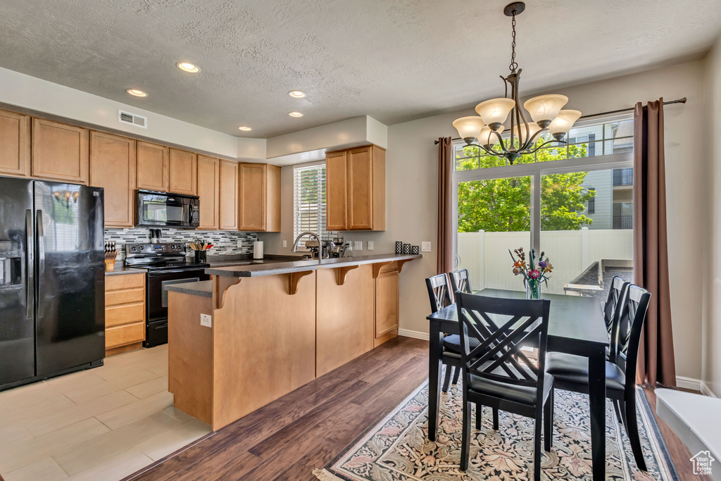 Kitchen with black appliances, a textured ceiling, a breakfast bar, a chandelier, and a peninsula