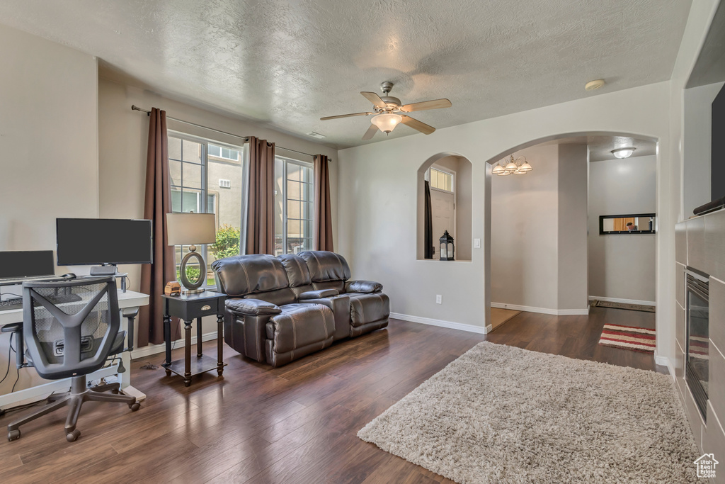 Living area featuring arched walkways, a textured ceiling, ceiling fan, dark wood-type flooring, and baseboards