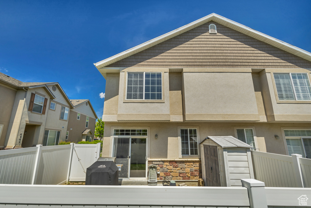 Rear view of property featuring a fenced backyard, a storage unit, stucco siding, an outdoor structure, and stone siding