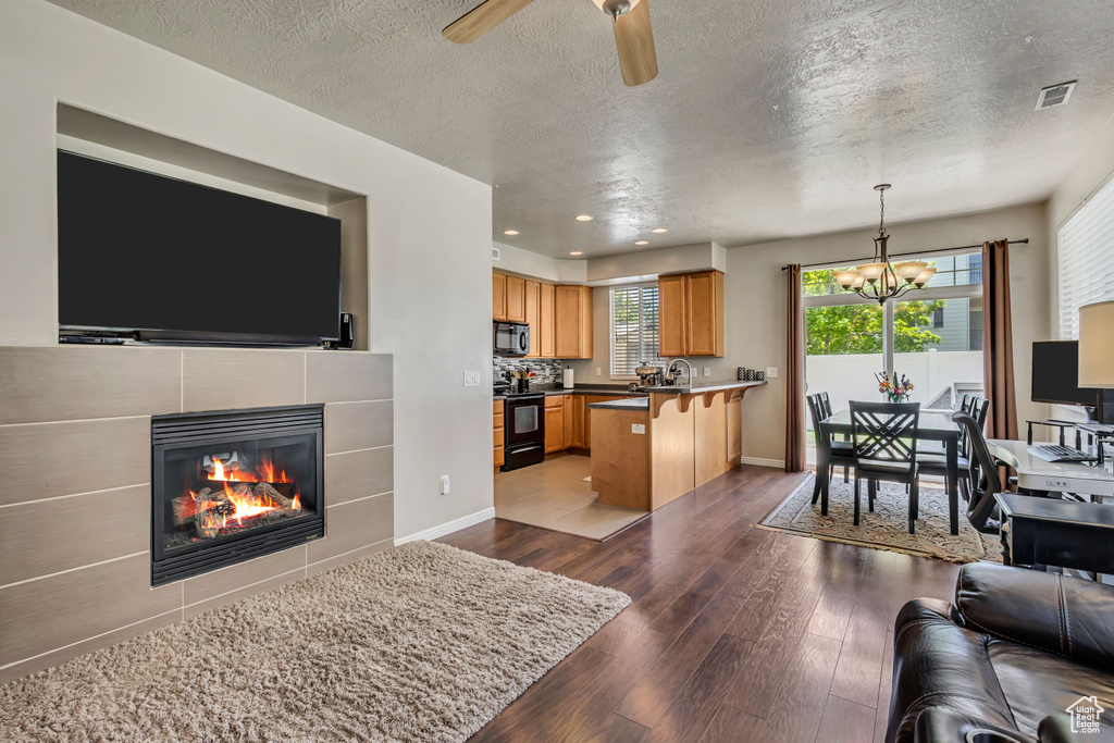 Living room with dark wood-type flooring, a chandelier, a textured ceiling, a fireplace, and recessed lighting
