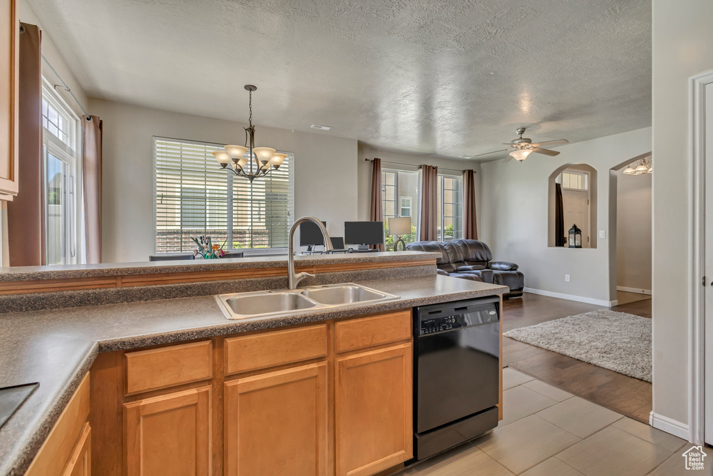 Kitchen featuring dishwasher, a sink, open floor plan, a chandelier, and a textured ceiling