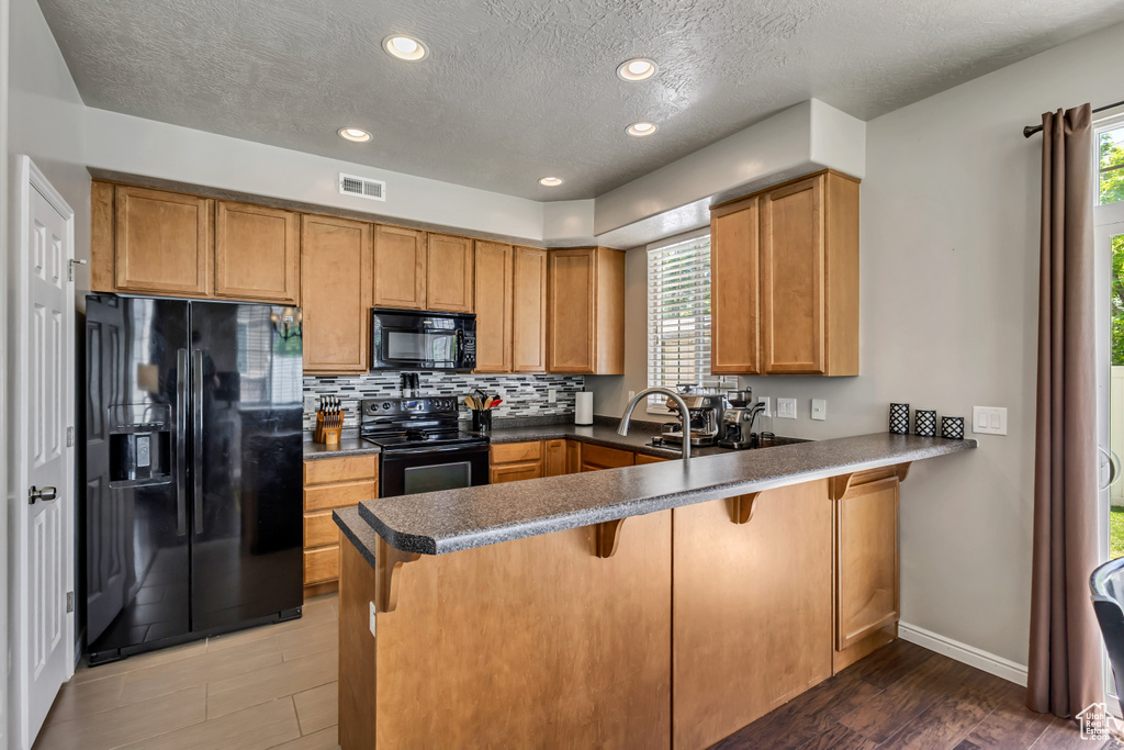 Kitchen featuring black appliances, a peninsula, brown cabinetry, a kitchen breakfast bar, and backsplash