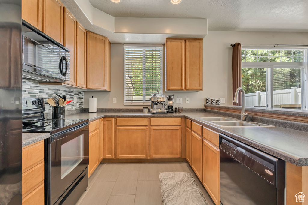 Kitchen featuring black appliances, a sink, decorative backsplash, and light tile patterned flooring