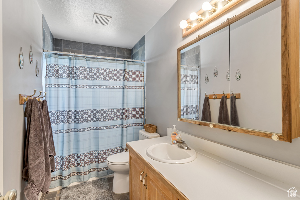 Full bath featuring vanity, a textured ceiling, a shower with curtain, and toilet