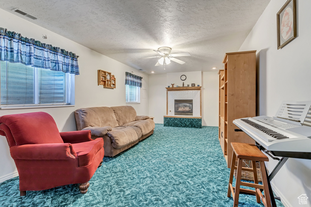 Carpeted living room with a textured ceiling, ceiling fan, and a tile fireplace