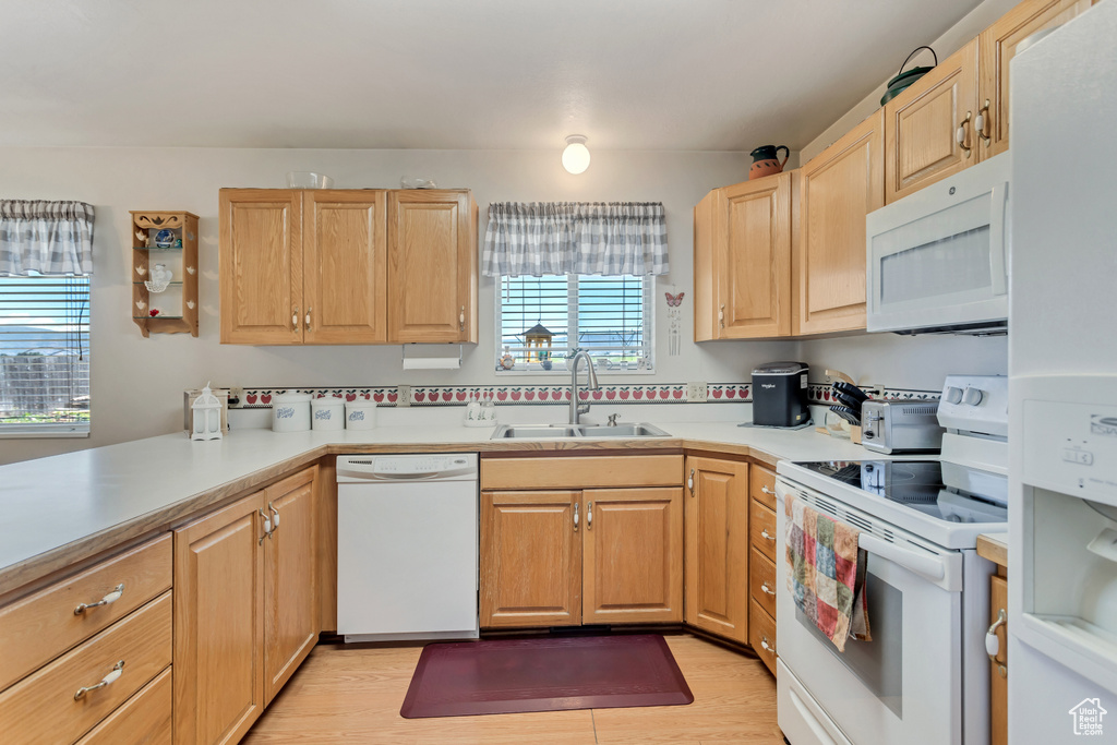 Kitchen with white appliances, a sink, light countertops, and light wood-style flooring