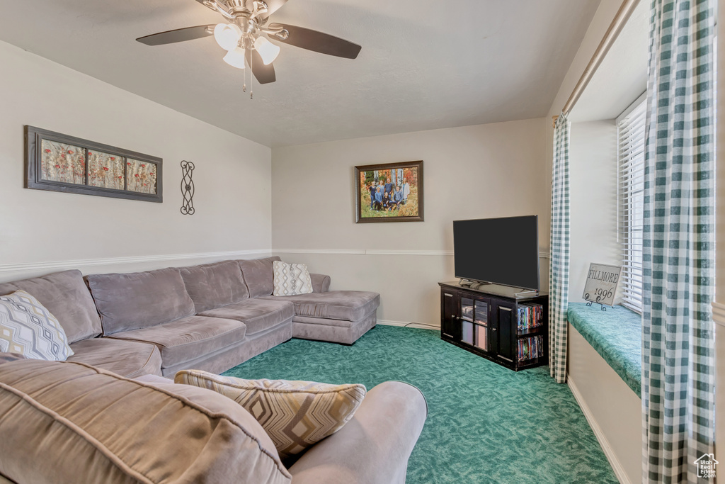 Carpeted living room featuring ceiling fan and baseboards