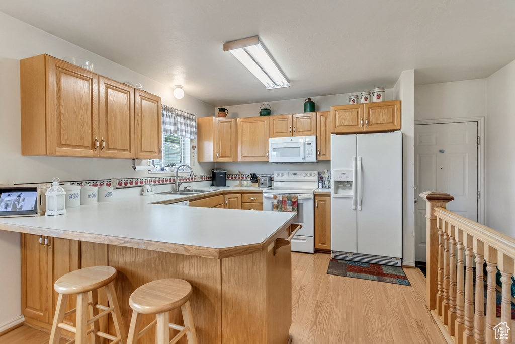 Kitchen featuring white appliances, light wood-style flooring, a sink, and a peninsula