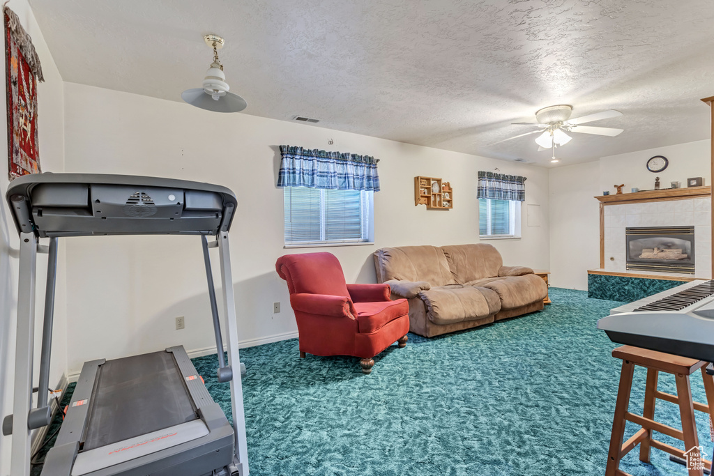 Living area featuring carpet flooring, ceiling fan, a textured ceiling, a tiled fireplace, and baseboards
