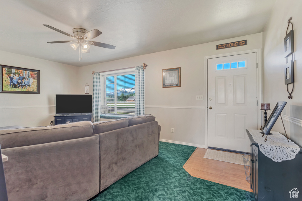 Living room with ceiling fan, dark carpet, and baseboards