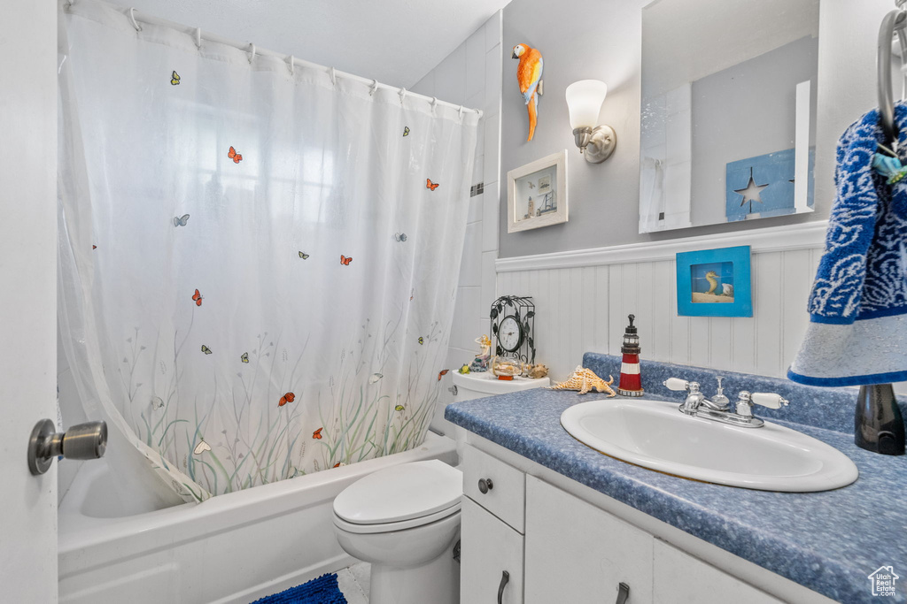 Full bathroom with shower / tub combo with curtain, vanity, toilet, and a wainscoted wall