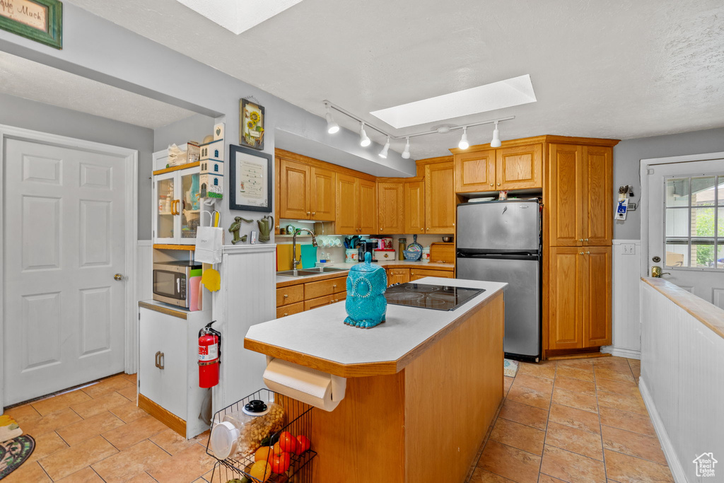 Kitchen featuring appliances with stainless steel finishes, a skylight, light countertops, a sink, and a center island