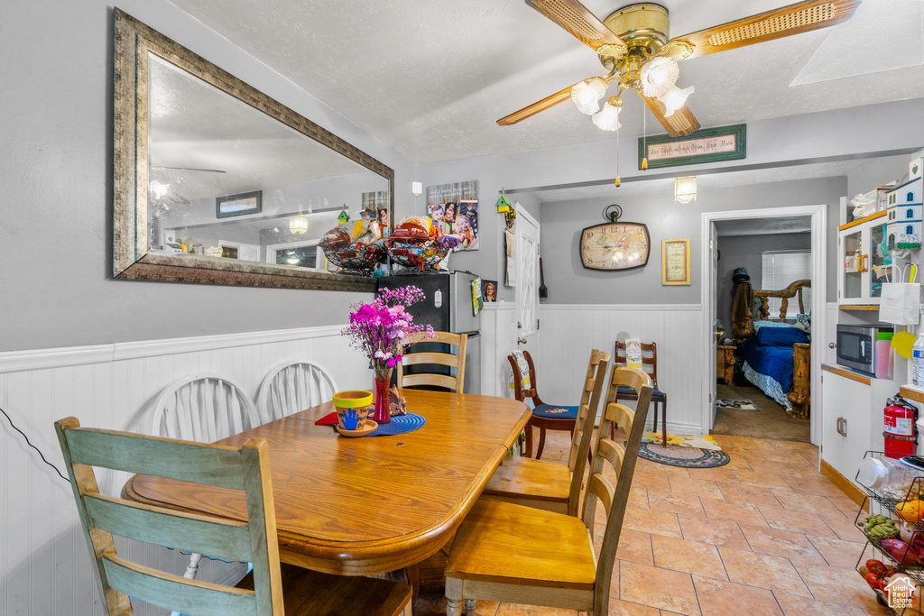 Dining space featuring a ceiling fan, wainscoting, and stone tile floors