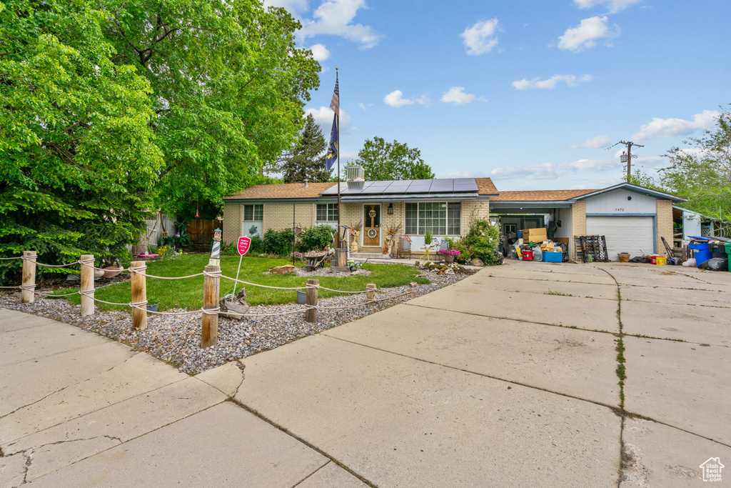 Ranch-style home featuring brick siding, a garage, roof mounted solar panels, concrete driveway, and a front lawn