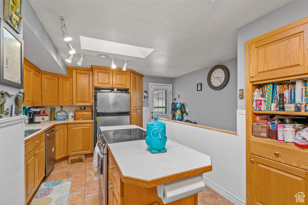 Kitchen with a skylight, appliances with stainless steel finishes, a kitchen island, light countertops, and wainscoting