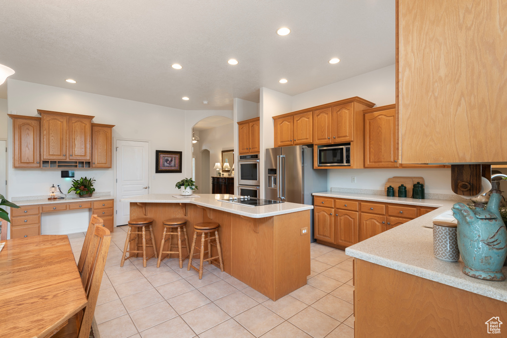 Kitchen featuring appliances with stainless steel finishes, arched walkways, a kitchen island, a kitchen bar, and recessed lighting