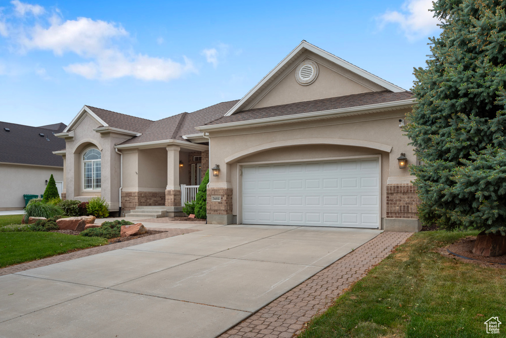View of front of home with stucco siding, concrete driveway, an attached garage, and brick siding