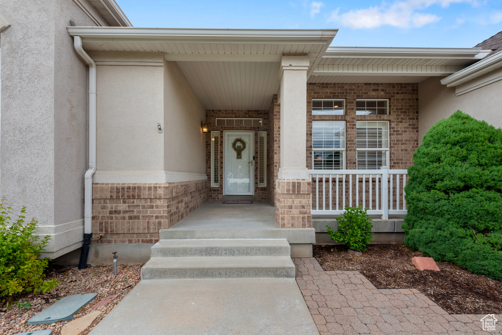 Entrance to property featuring brick siding, stucco siding, and covered porch