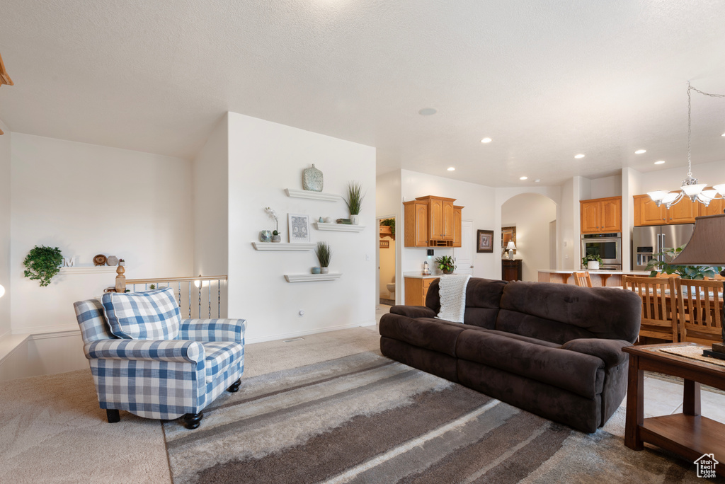 Carpeted living room with arched walkways, a chandelier, and recessed lighting