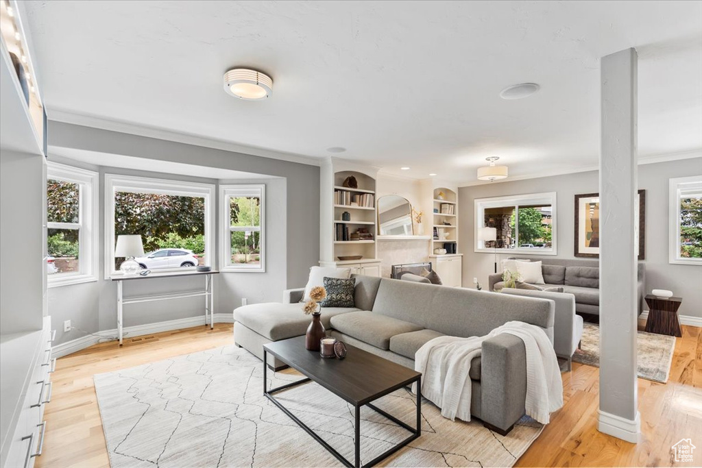 Living room featuring ornamental molding, light wood finished floors, a tiled fireplace, baseboards, and built in shelves