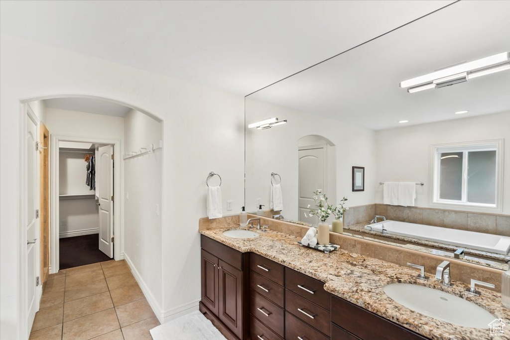 Full bathroom featuring tile patterned flooring, double vanity, a walk in closet, a bathtub, and baseboards