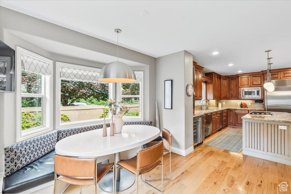 Kitchen featuring built in appliances, wine cooler, light wood-type flooring, hanging light fixtures, and a sink