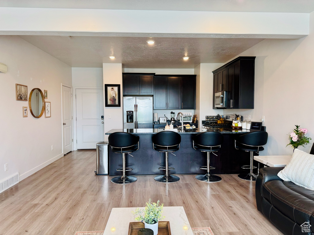 Kitchen with stainless steel appliances, a peninsula, a breakfast bar area, light wood-style flooring, and a sink
