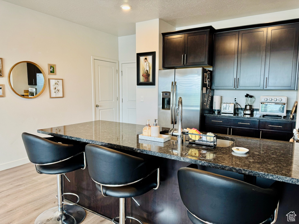 Kitchen with stainless steel fridge, dark stone countertops, a breakfast bar area, and light wood-type flooring
