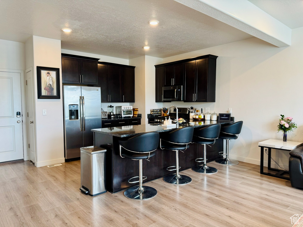Kitchen featuring appliances with stainless steel finishes, a peninsula, light wood-type flooring, baseboards, and recessed lighting