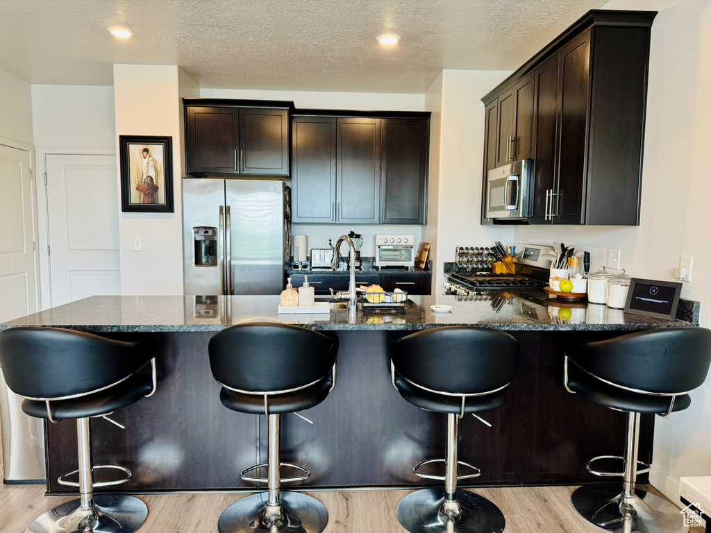 Kitchen featuring stainless steel appliances, dark stone countertops, dark brown cabinetry, a textured ceiling, and recessed lighting