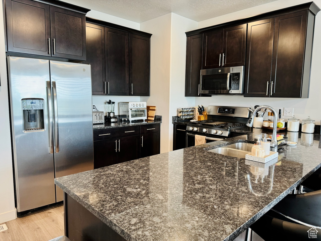 Kitchen featuring appliances with stainless steel finishes, a sink, dark stone countertops, light wood-type flooring, and a peninsula