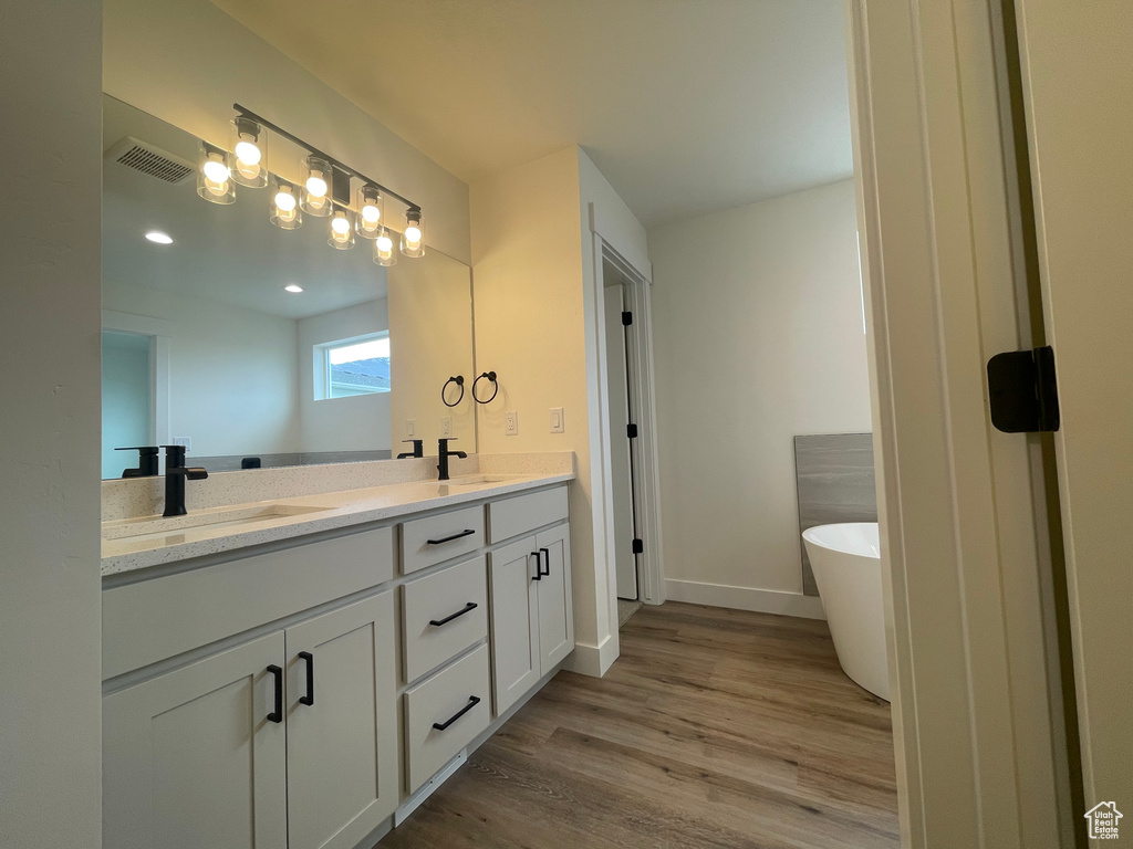 Full bathroom featuring wood finished floors, double vanity, a soaking tub, and baseboards